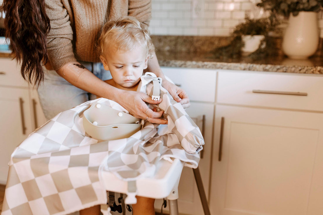 An adult fitting a Bibvy bib with adjustable buckles on a pensive toddler, showcasing the ease of putting on the bib for a snug fit.