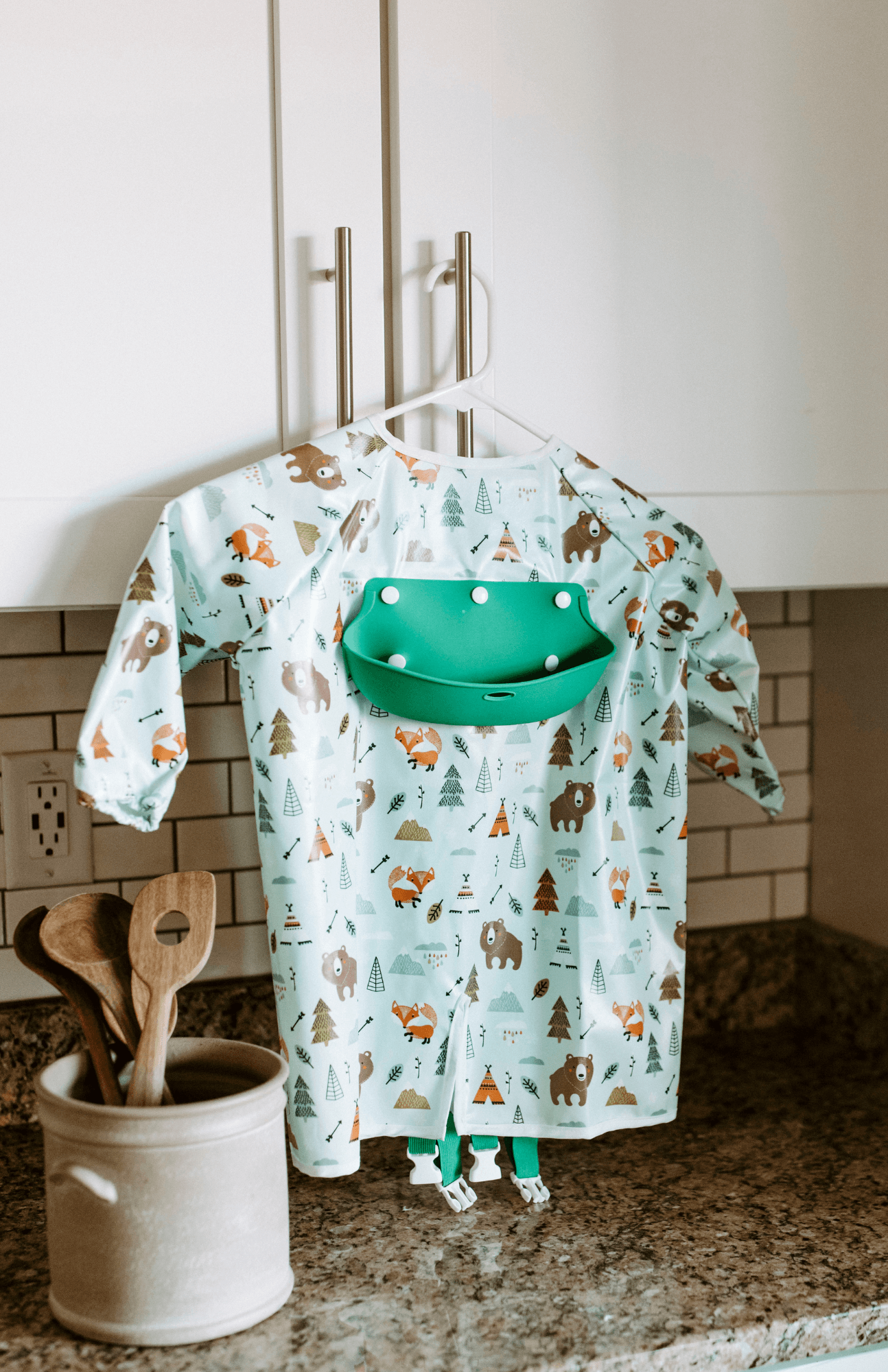 Wilderness Wonder print long sleeve Bibvy bib with a vibrant green food catcher, displayed in a homey kitchen setting.